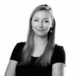 Krystian Cieślik na szarobiałym tle, ubrany w białą koszulę, wskazującego palcem na obiektyw aparatu.